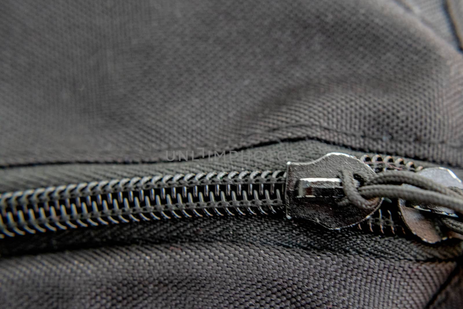 A close-up view of a black zipper shows the teeth and detail of its stitching into the fabric of a backpack.