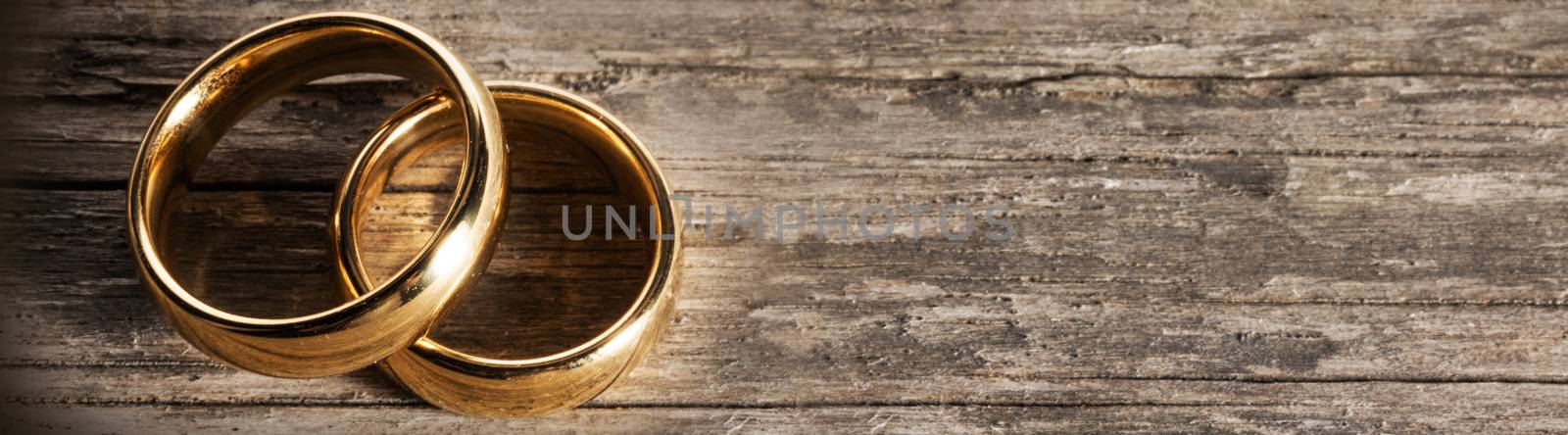 Two golden wedding rings on wooden background with copy space for text