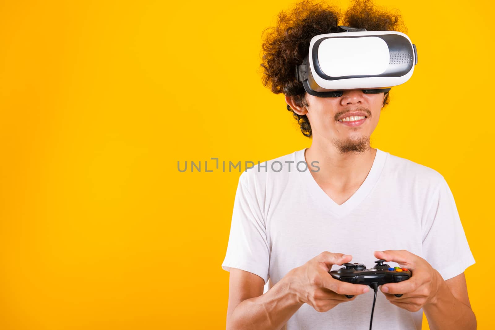 Asian handsome man with curly hair play game he using virtual reality headset or VR glass isolate on yellow background with copy space for text