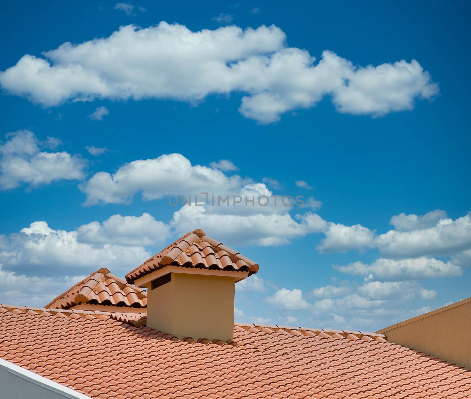 A red tile roof and dormer against a bright blue sky