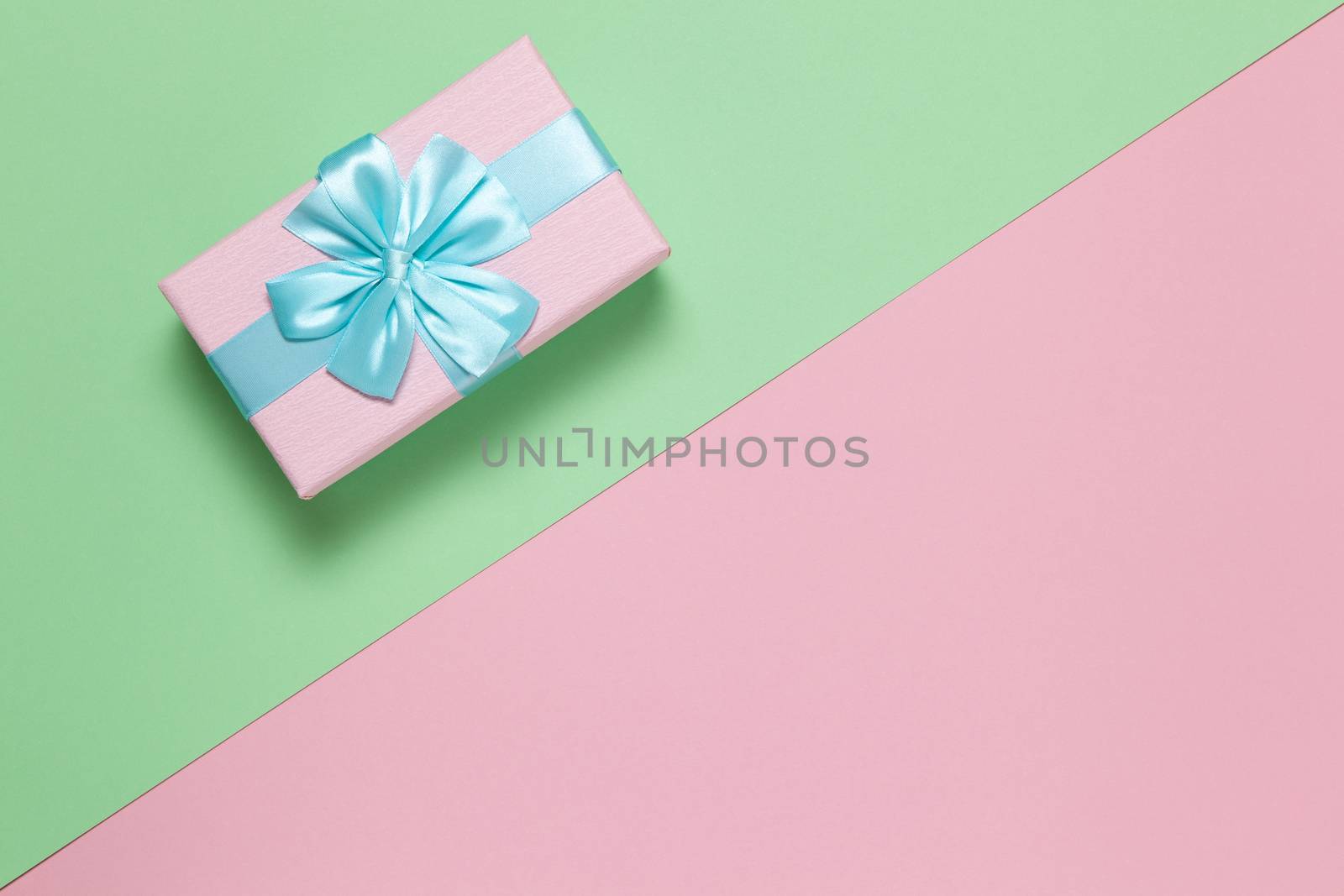 Pink gift box with blue bow on pastel two-color background pink and green, copy space, flat lay. March 8, February 14, birthday, St. Valentine's, Mother's, Women's day celebration concept. Horizontal.