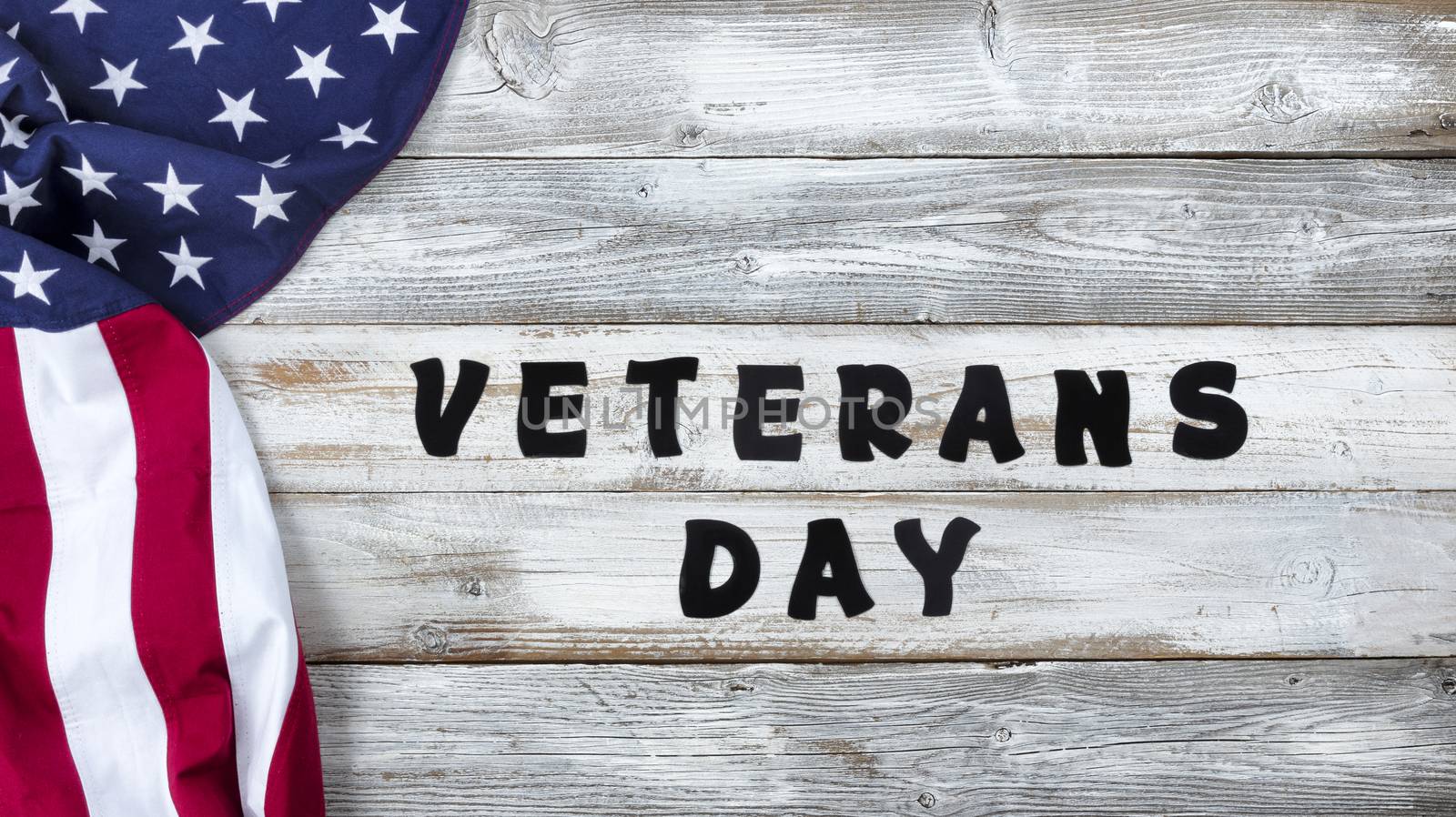Waving United States Flag on left side of white rustic wooden background with large text for Veterans Day 
