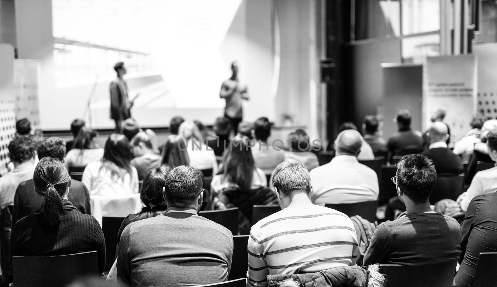 Speaker giving a talk in conference hall at business event. Audience at the conference hall. Business and Entrepreneurship concept. Focus on unrecognizable people in audience. Black and white image.