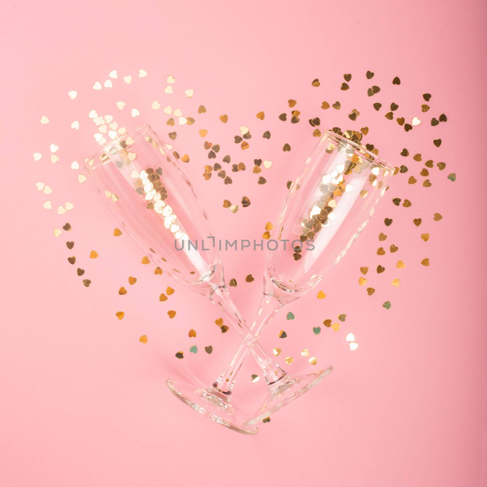 Valentines day champagne flutes glasses and heart shaped golden glitters on pink background with copy space for text