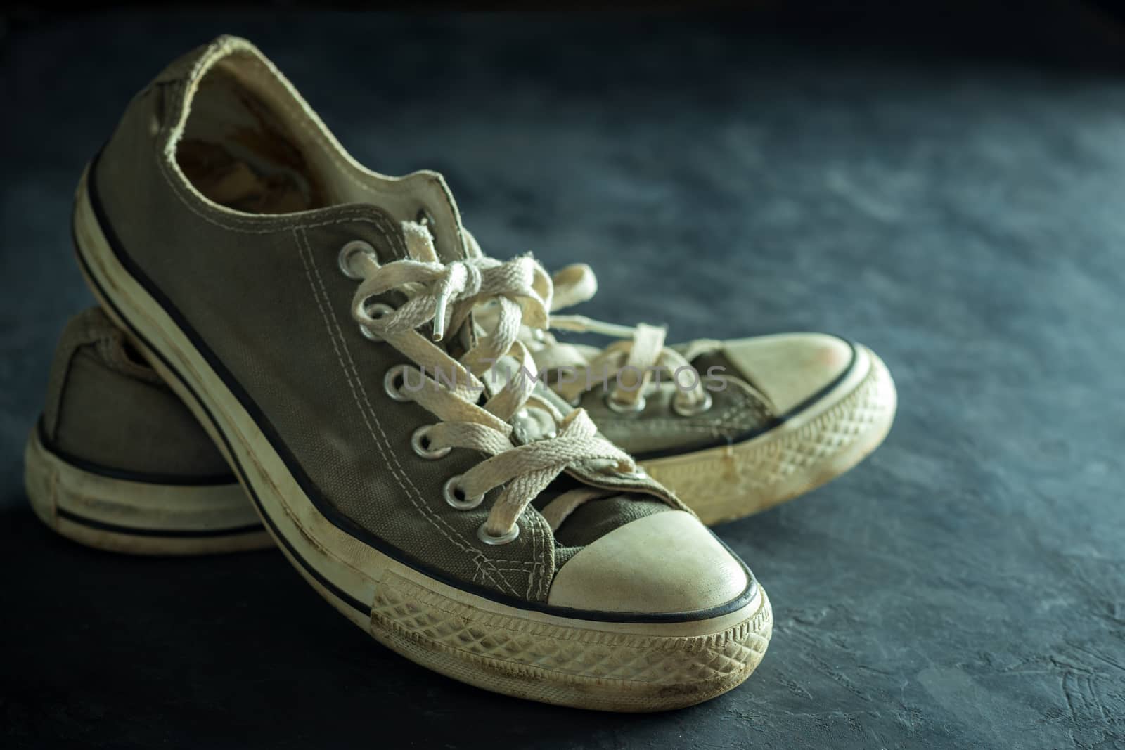 Dirty sneaker in darkness. Closeup old sneaker on black cement floor. Copy space for text. Concept of traveling.