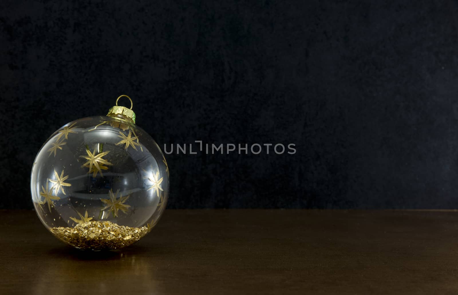 transparent christmas ball with gold colored glitters on a dark black background for christmas card