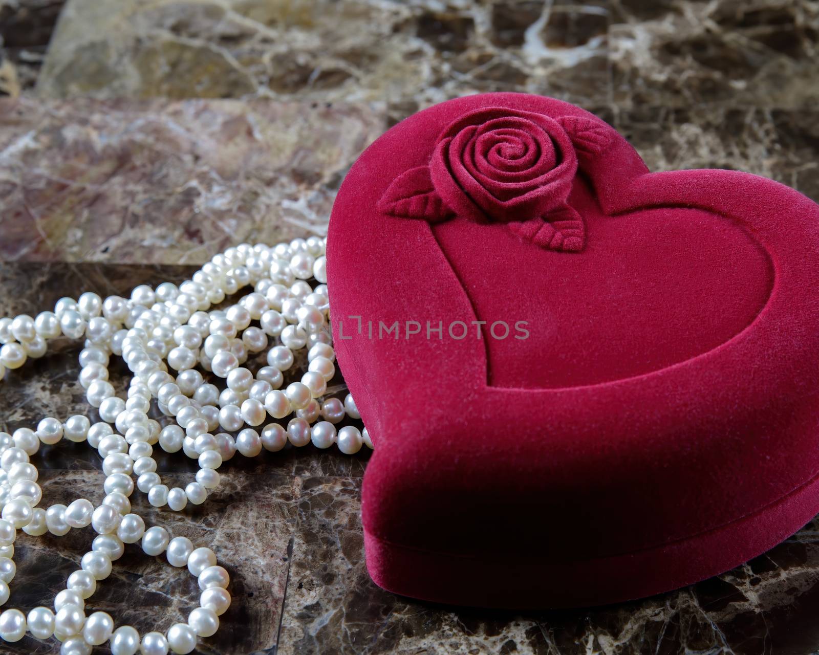 Pearl necklace in a red heart-shaped gift box on a marble background. Close-up. Happy birthday or mother's day. A romantic gift for Valentine's Day or for a wedding