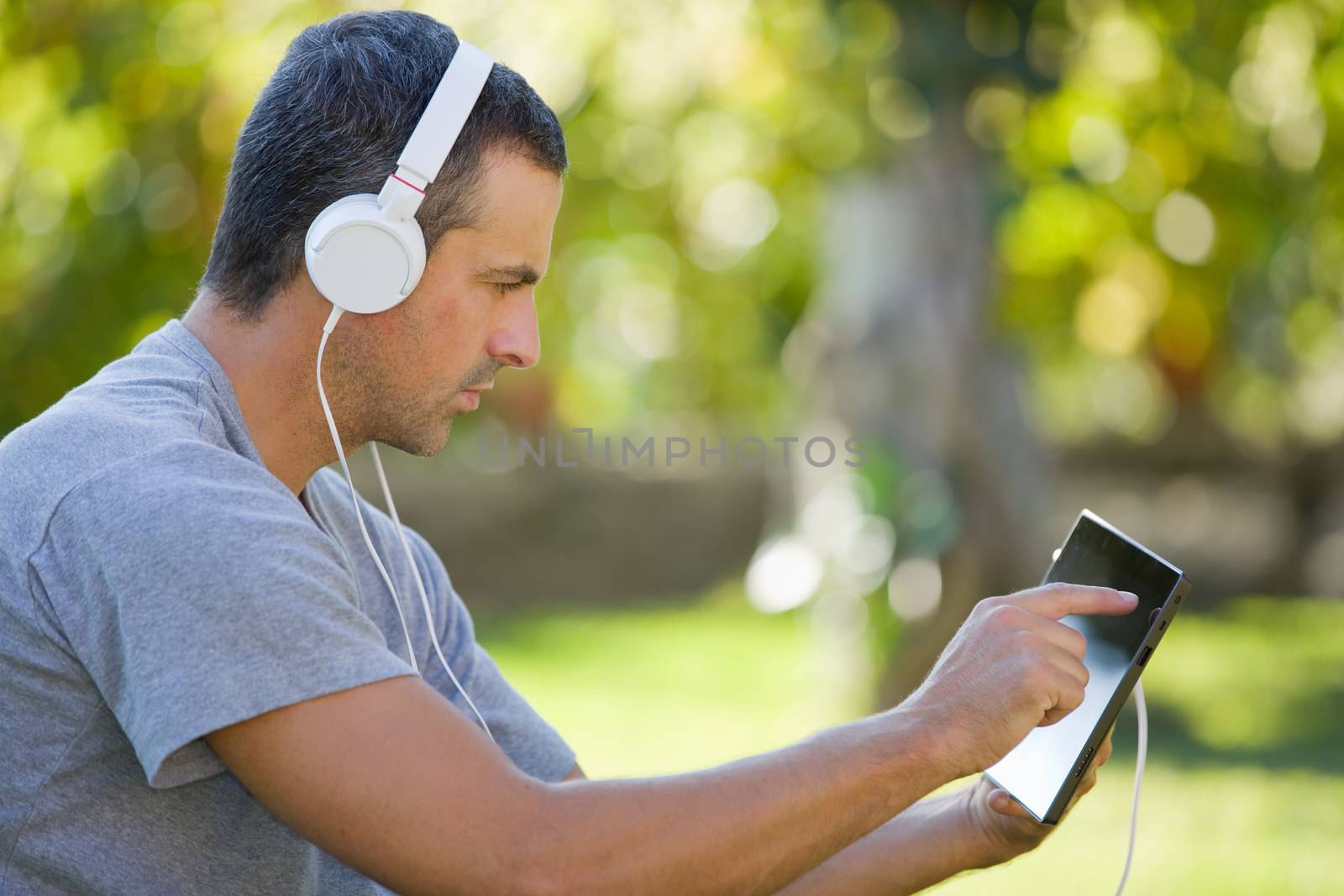 young man relaxing with a tablet pc listening music with headphones on a the park, outdoor