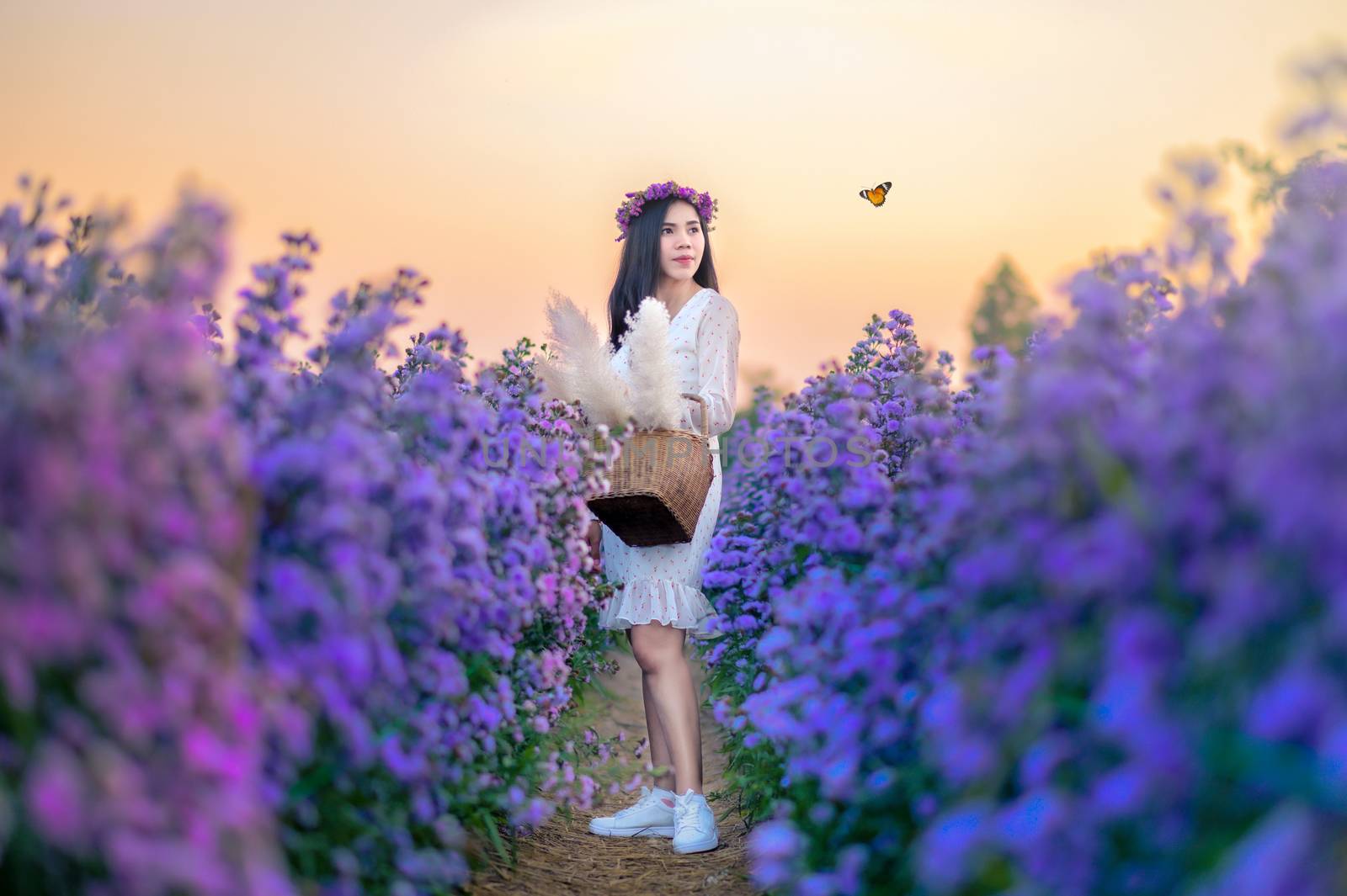 A woman watching flowers in a flower field with butterflies in the evening, orange light.