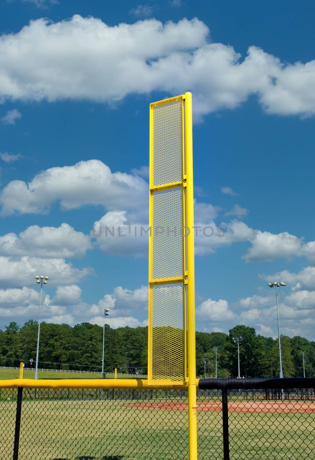 A bright yellow foul ball pole in a baseball field against blue sky