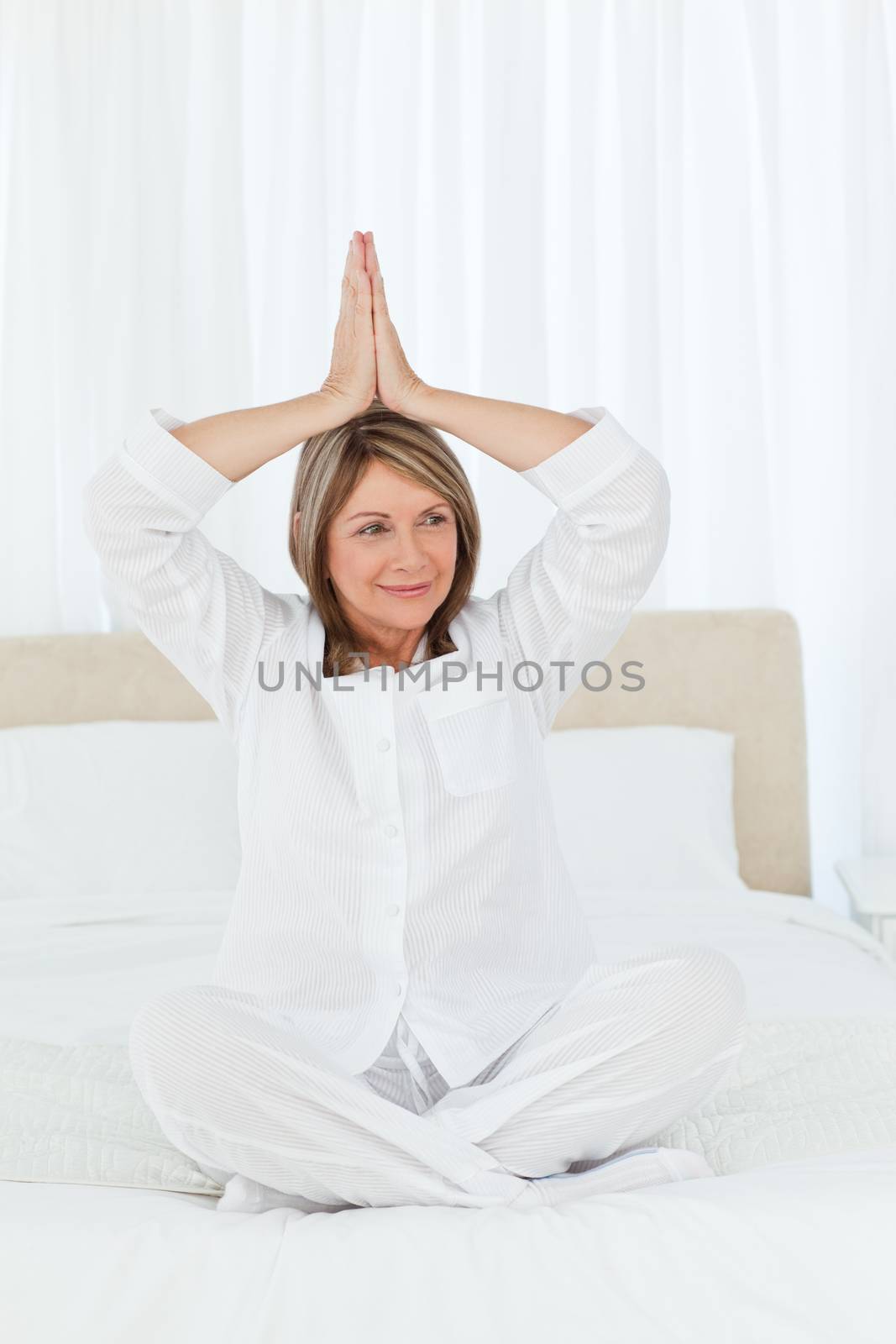 Senior practicing yoga on her bed by Wavebreakmedia