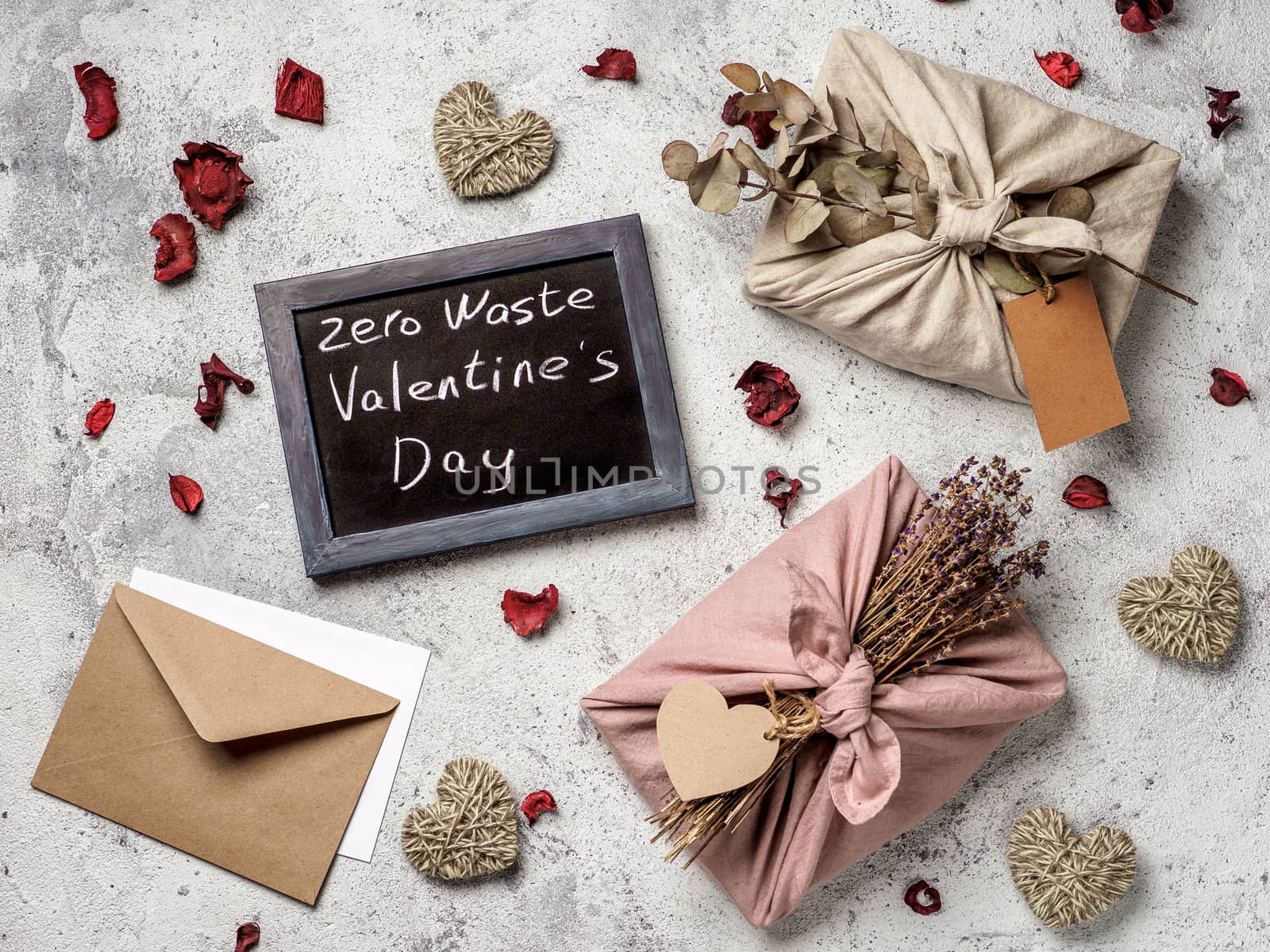 Zero waste Valentine's Day concept. Eco-friendly gift cloth wrapping in Furoshiki style and chalkboard with Zero Waste Valentine's Day letters on gray textured background. Top view or flat lay