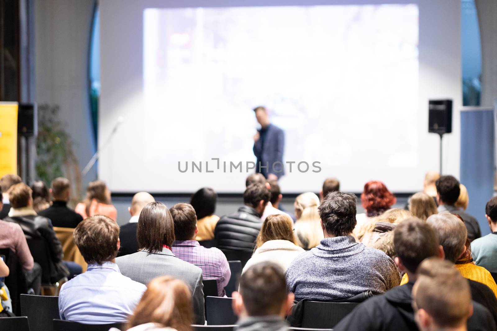 Speaker giving a talk in conference hall at business event. Audience at the conference hall. Business and Entrepreneurship concept. Focus on unrecognizable people in audience.