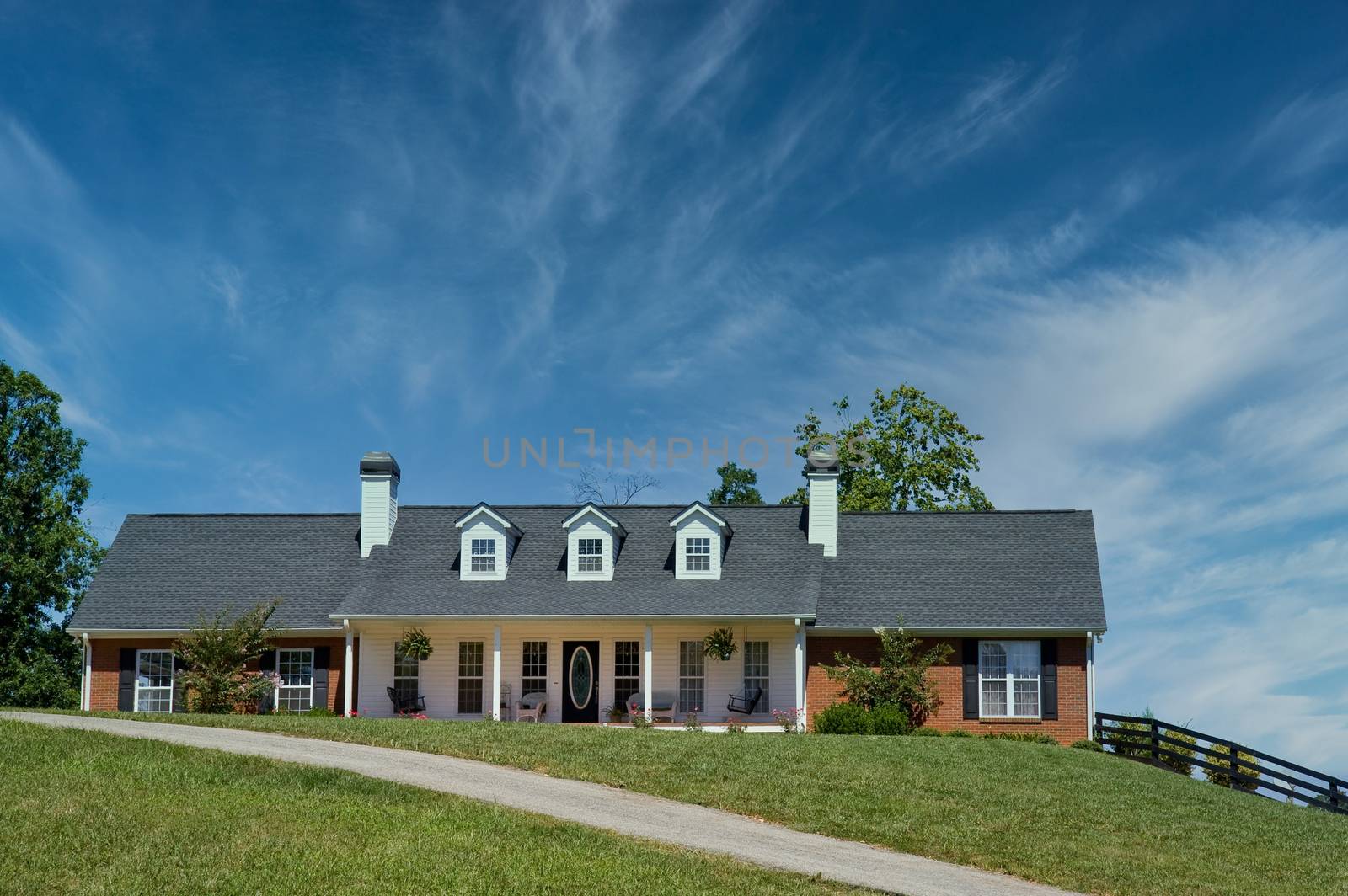 A nice brick ranch house on a grassy hill with blue sky