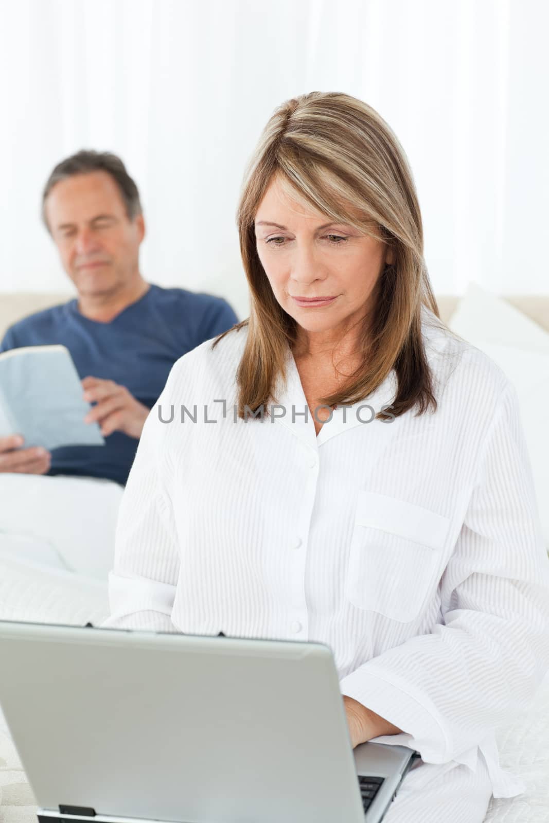 Woman looking at her laptop while her husband is reading by Wavebreakmedia