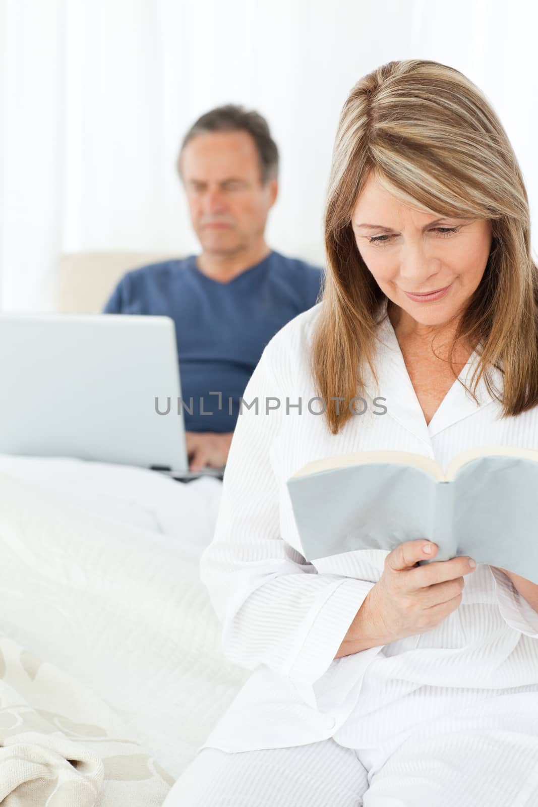 Man looking at his laptop while her wife is reading at home