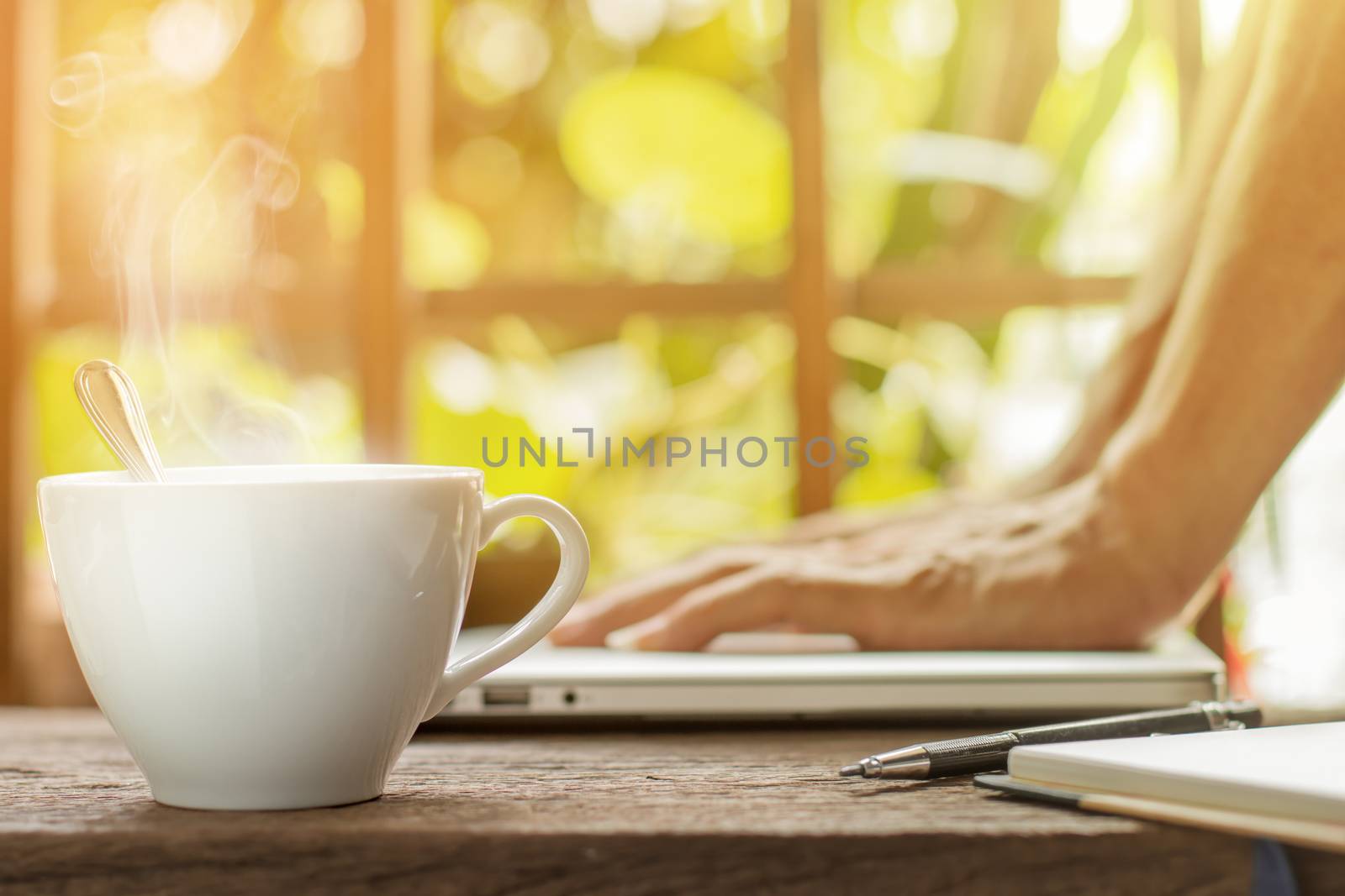 White hot coffee cup with businessman working laptop green garden background