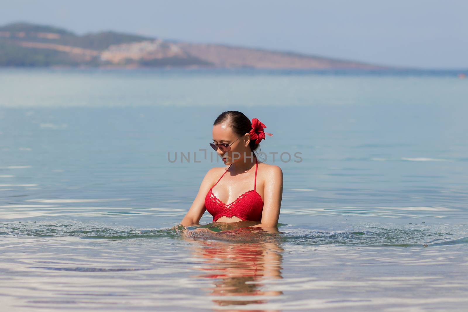 Beautiful woman walking in sea waterLovely young lady in red knitted swimwear looking away and walking in sea water while relaxing in wonderful resort