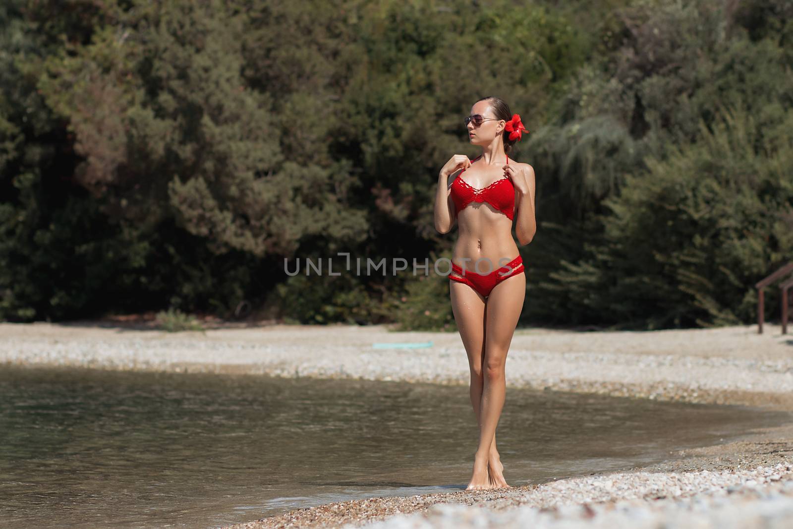 Beautiful woman walking in sea waterLovely young lady in red knitted swimwear looking away and walking in sea water while relaxing in wonderful resort