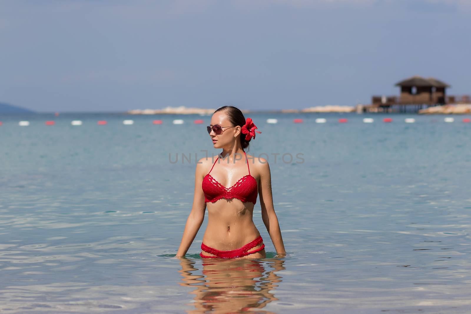 Beautiful woman walking in sea waterLovely young lady in red knitted swimwear looking away and walking in sea water while relaxing in wonderful resort