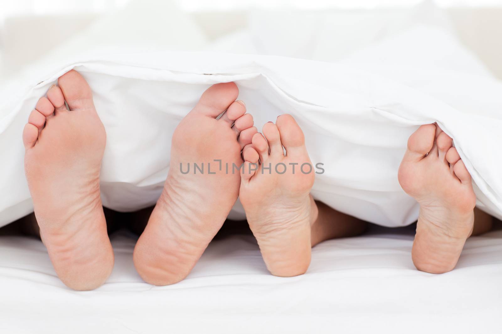 Two members of a family showing their feet while lying on a bed by Wavebreakmedia