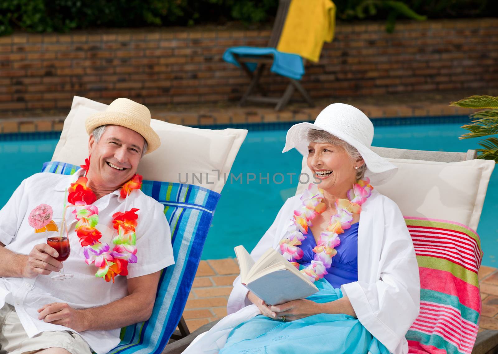 Mature woman reading a book while her husband is drinking a cocktail