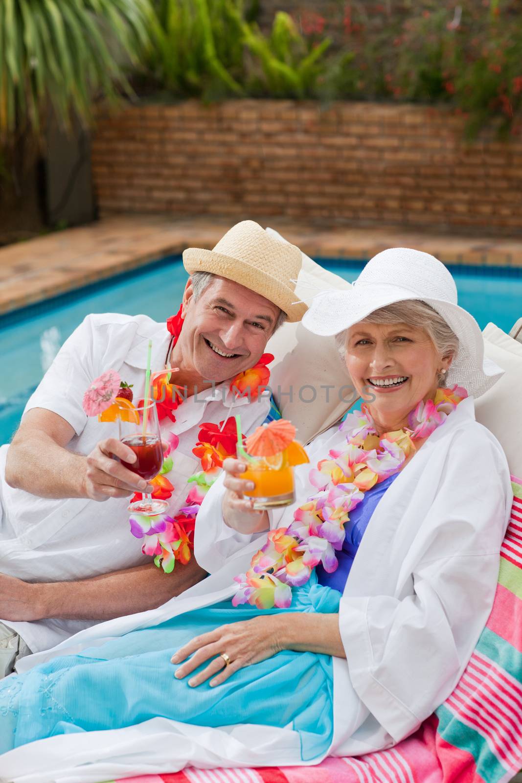 Mature couple drinking a cocktail beside the swimming pool