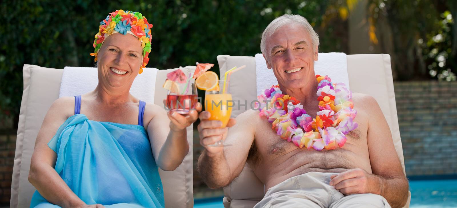 Mature couple drinking a cocktail beside the swimming pool at home