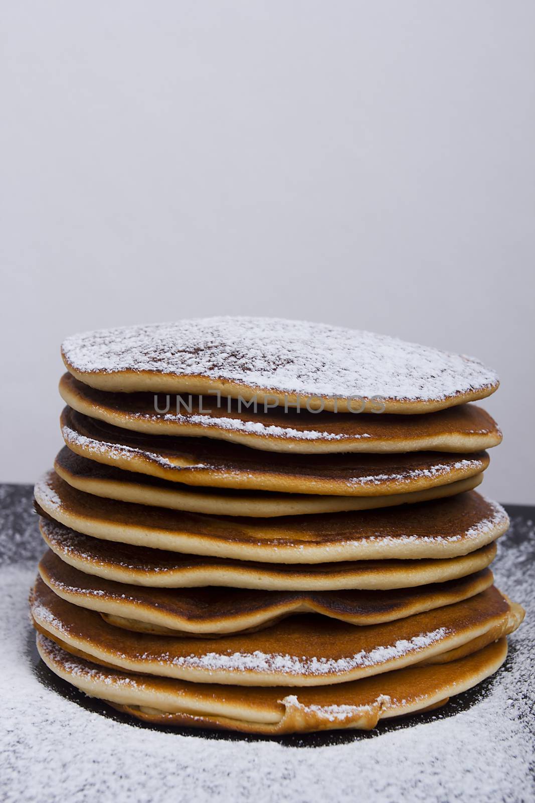 A stack of pancakes on a plate sprinkled with powdered sugar