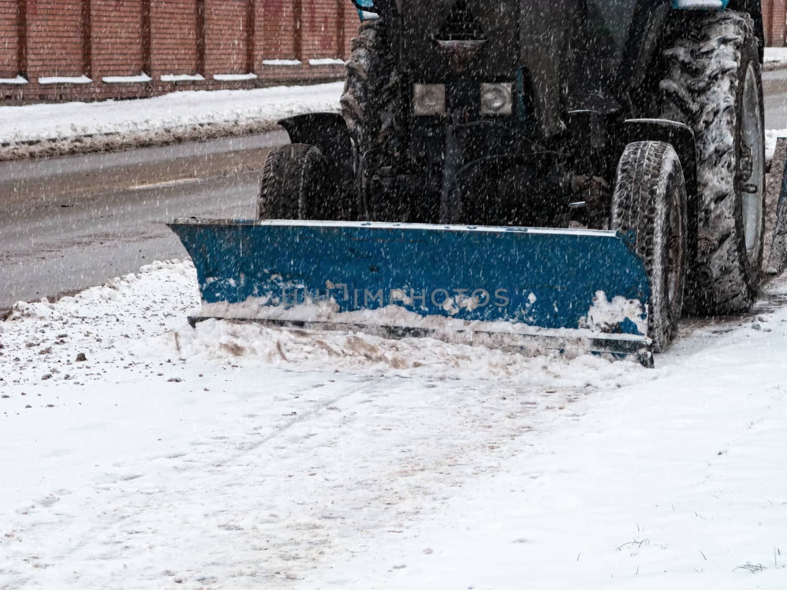 The tractor cleans the pavement from snow in winter with a snow blower and a rotating brush. Municipal services remove snow so as not to slip on the road. Snowing.