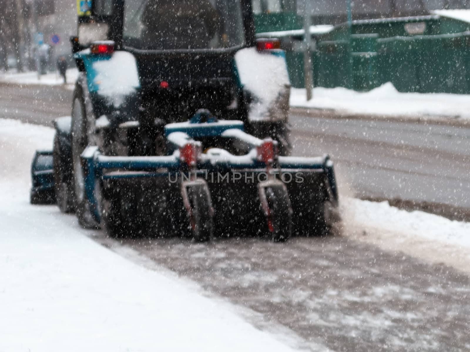 The tractor cleans the pavement from snow in winter with a snow blower and a rotating brush. Municipal services remove snow so as not to slip on the road. Snowing.