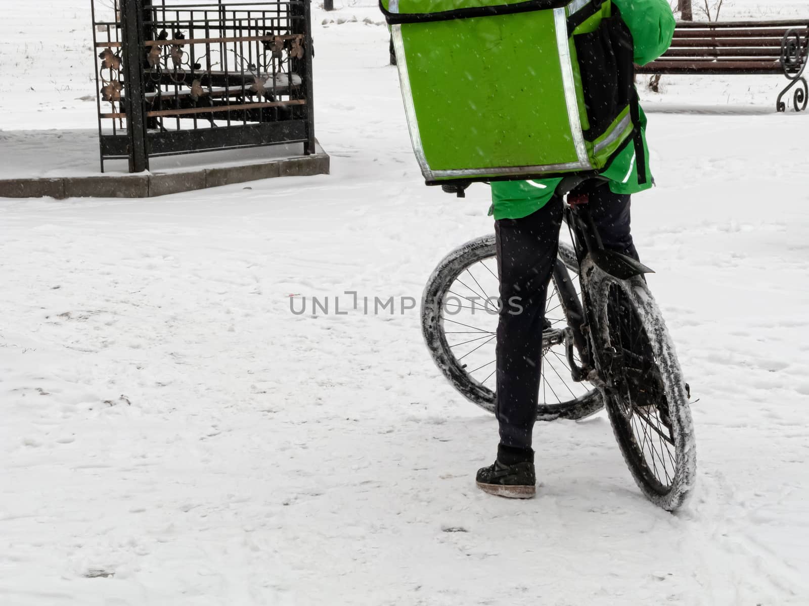 24-hour delivery service from cafes and restaurants. Take-away courier on a bike with a green isothermal backpack rides fast. Courier delivers food by bicycle in winter to avoid traffic jams