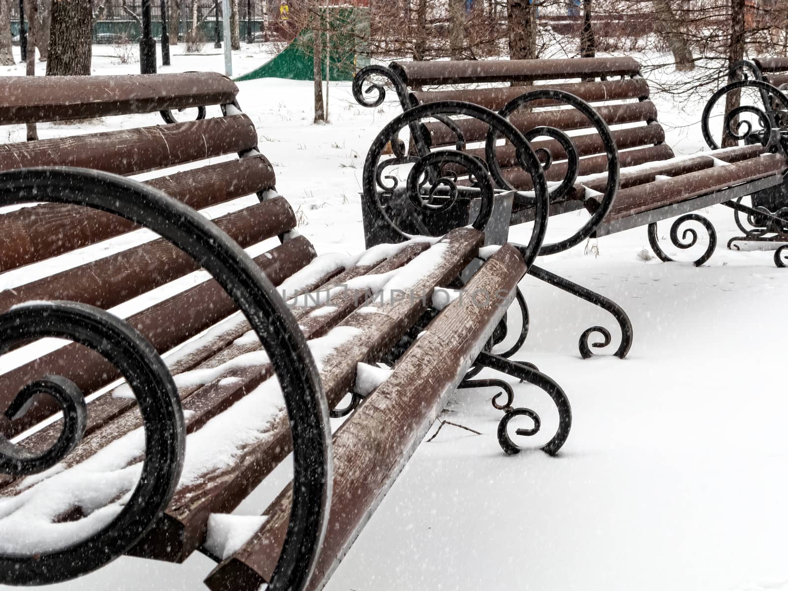 Empty red park benches covered in snow. Winter day in the park. Snowing.