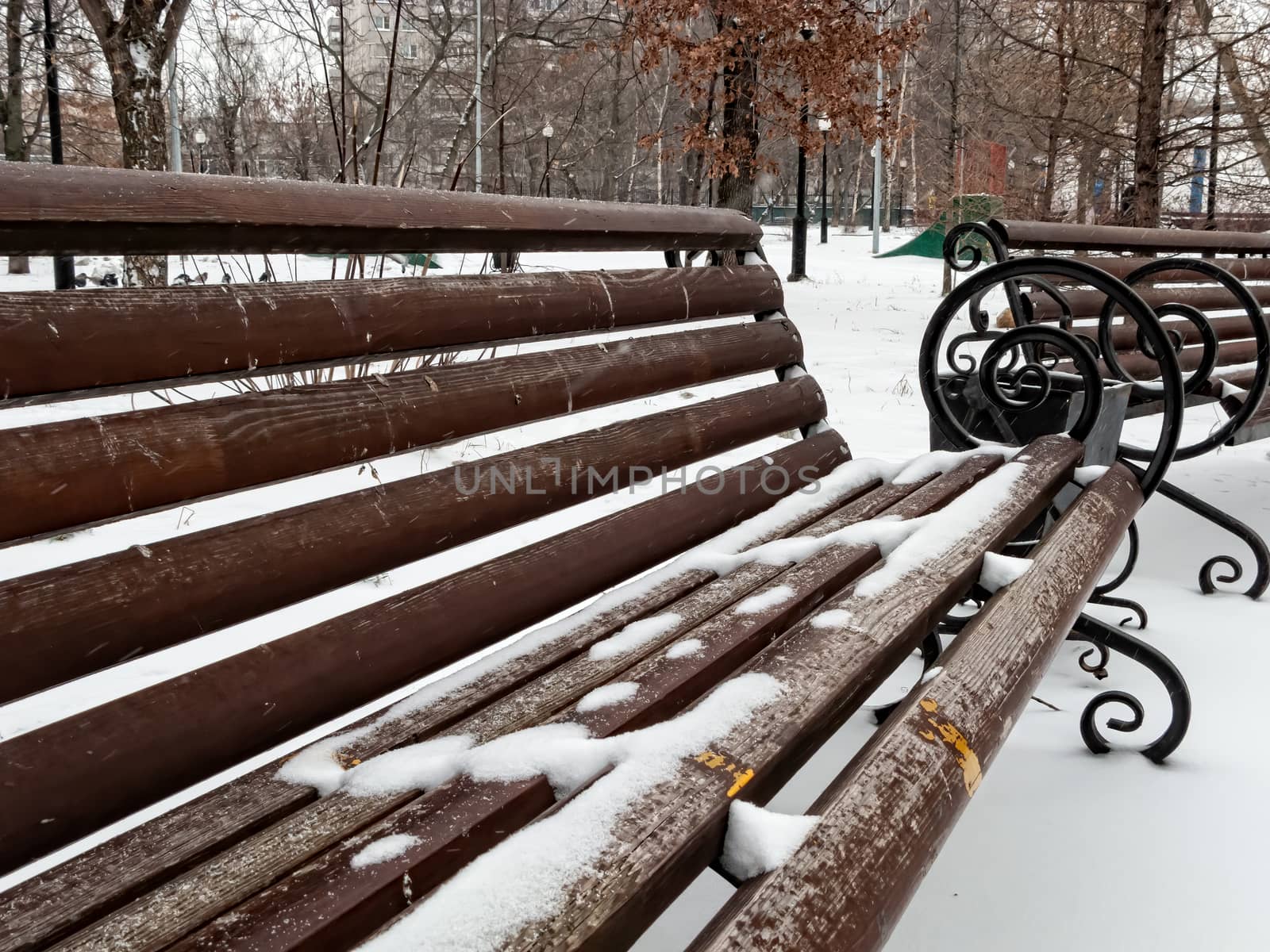 Empty red park benches covered in snow. Winter day in the park. Snowing.