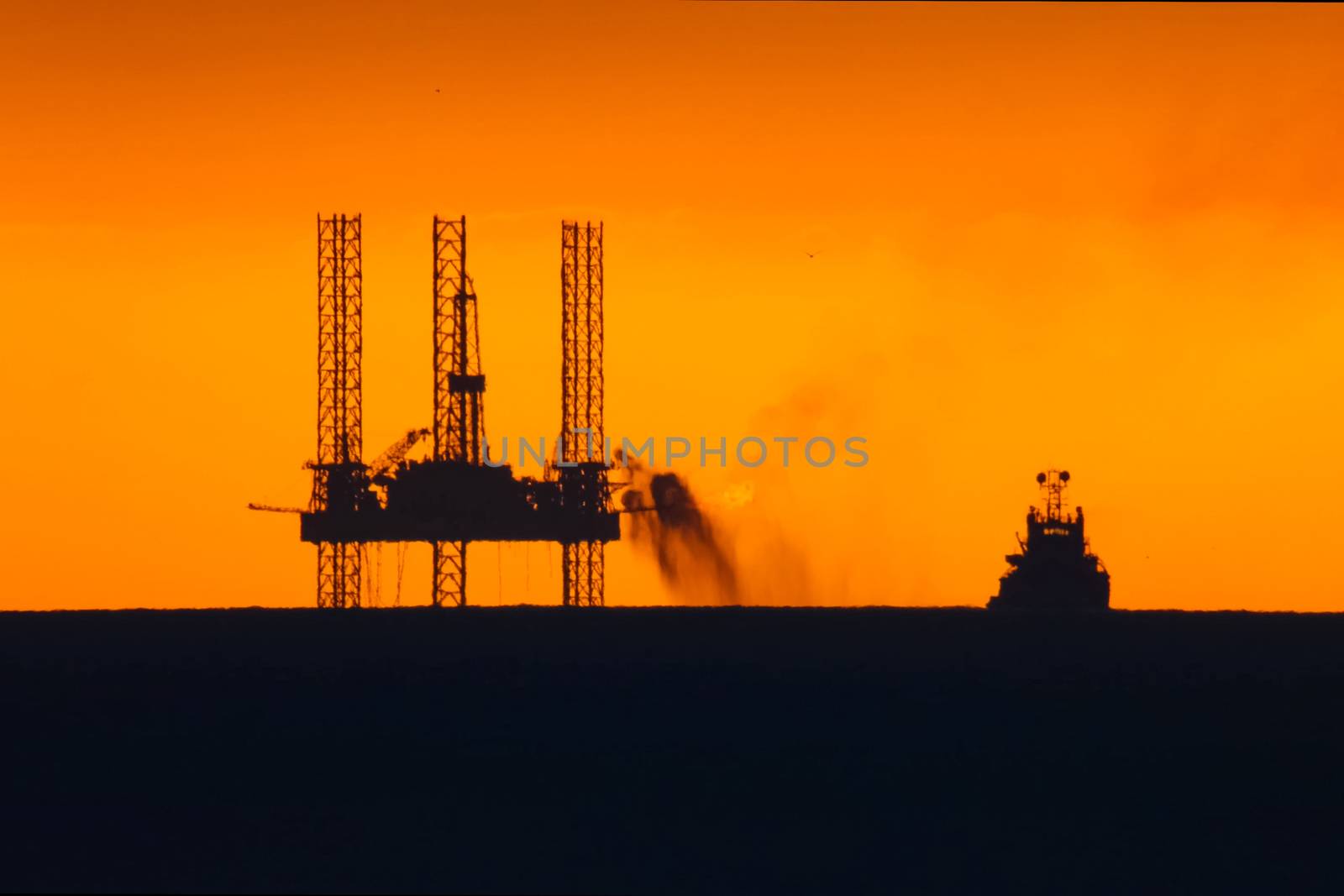 Drilling platform in the port. Oil platform at sunset with a burning torch. Towing of the oil platform.