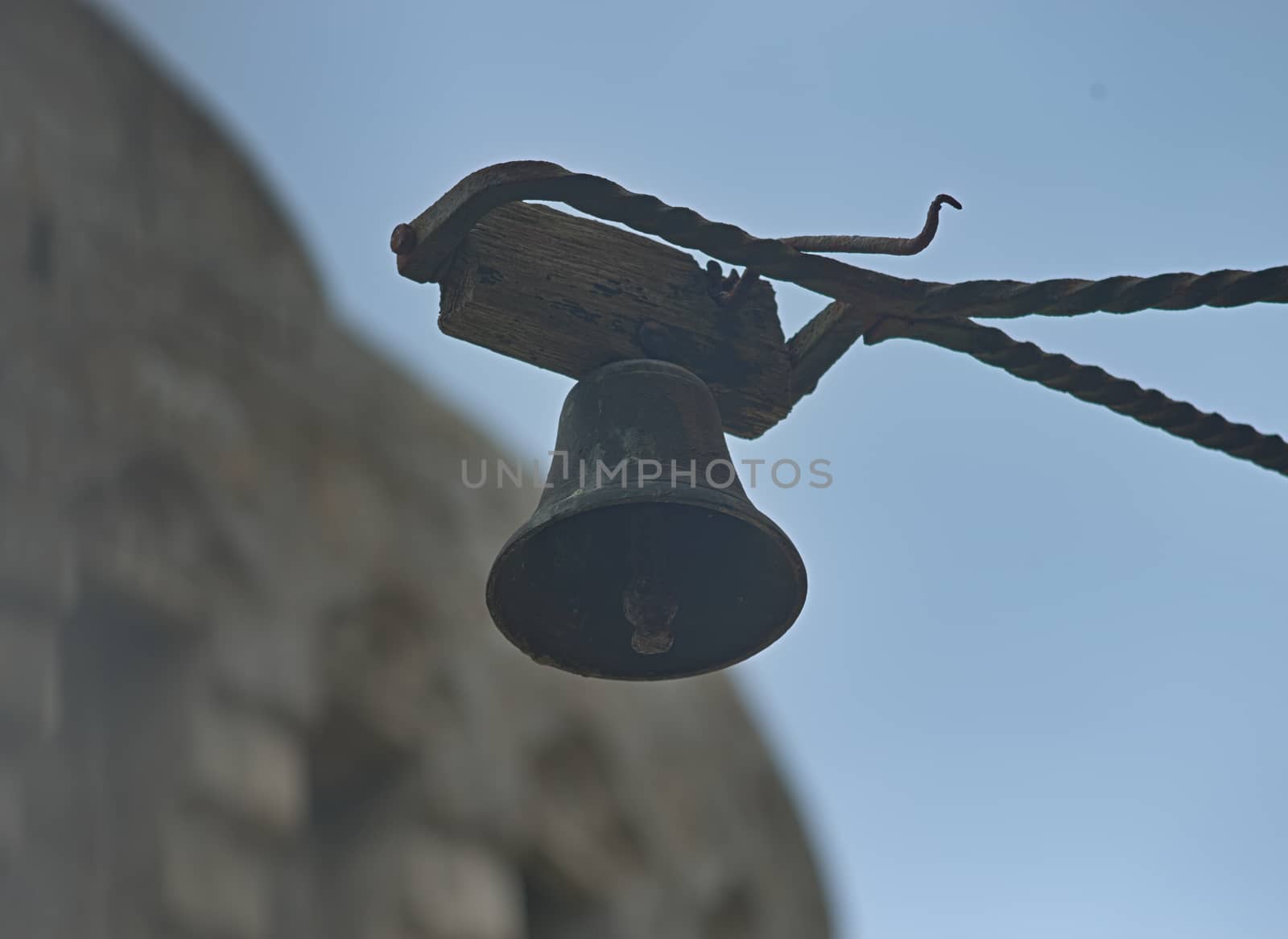 Small black bell hanging and sky and stone fortress in background