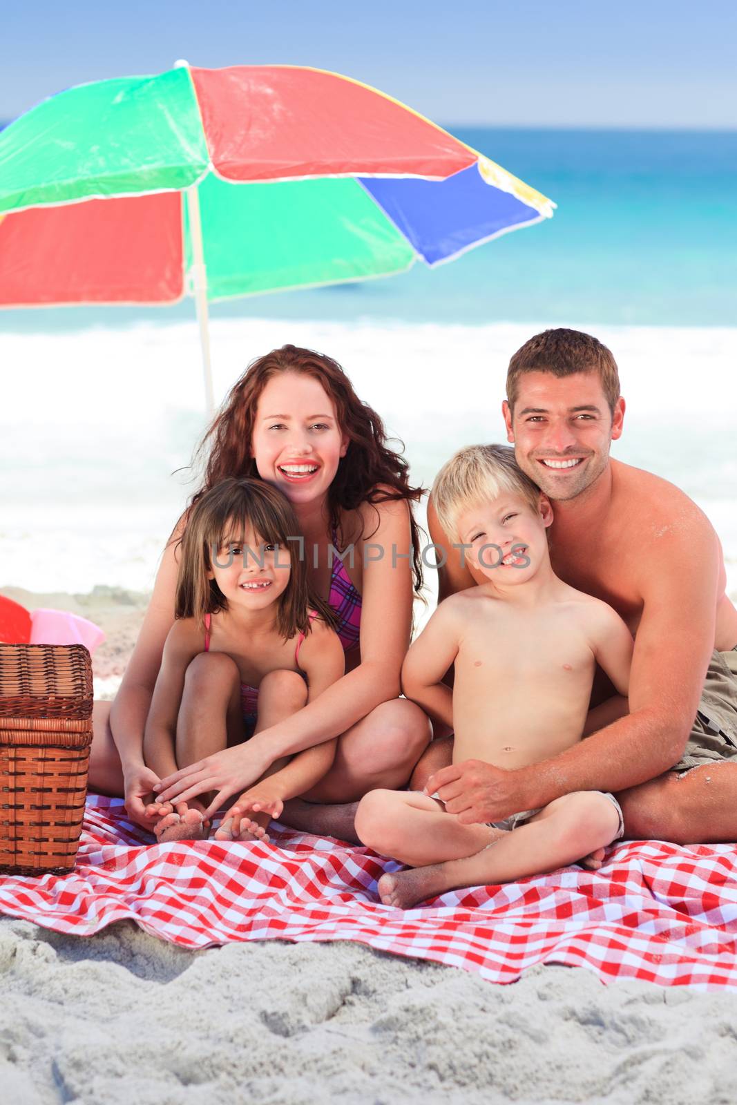 Family picnicking under a sol umbrella on the beach by Wavebreakmedia