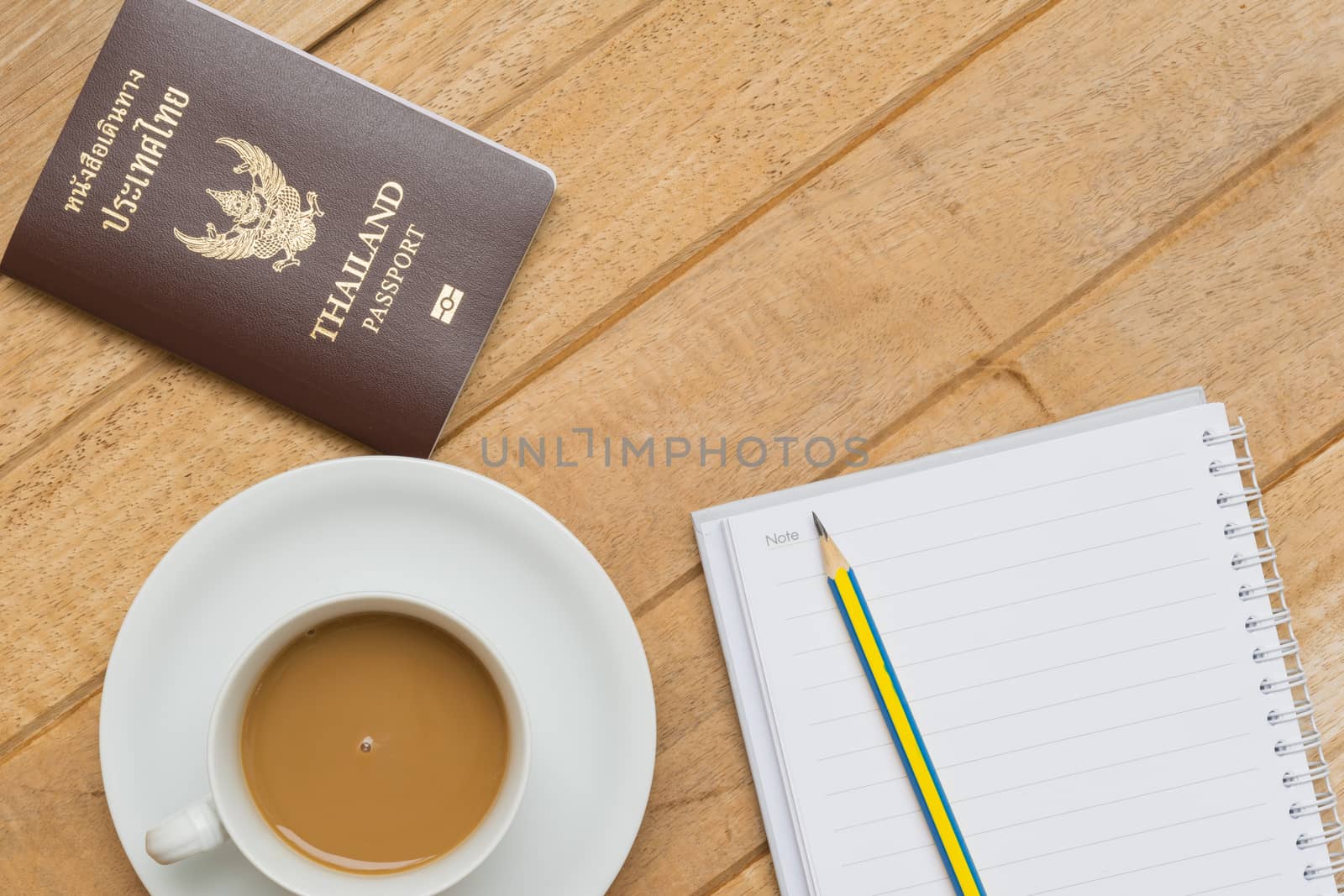 Top view of hot coffee on white cup, passport and pencil on notebook on wood textures is diagonal for background