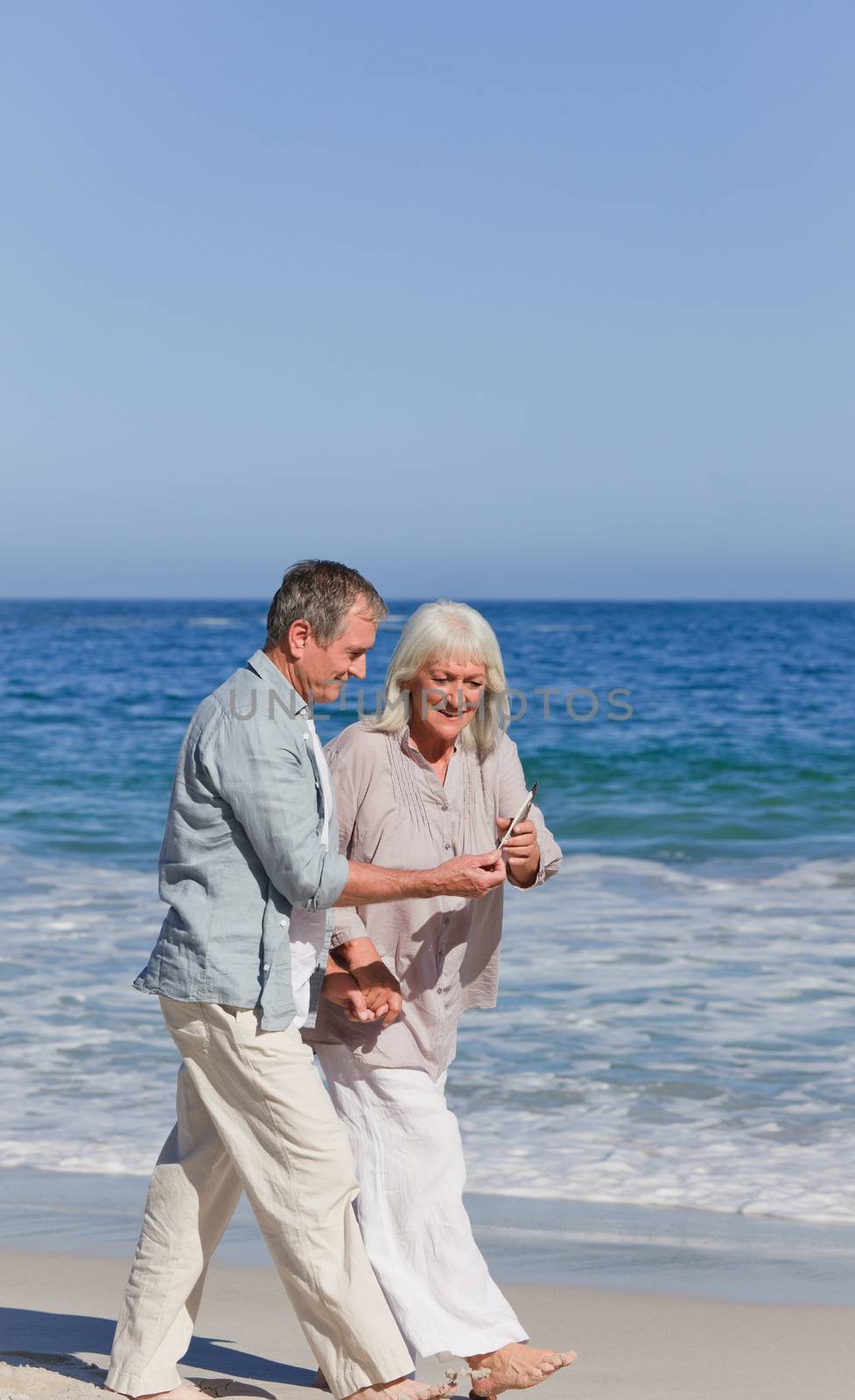 Elderly couple walking on the beach by Wavebreakmedia