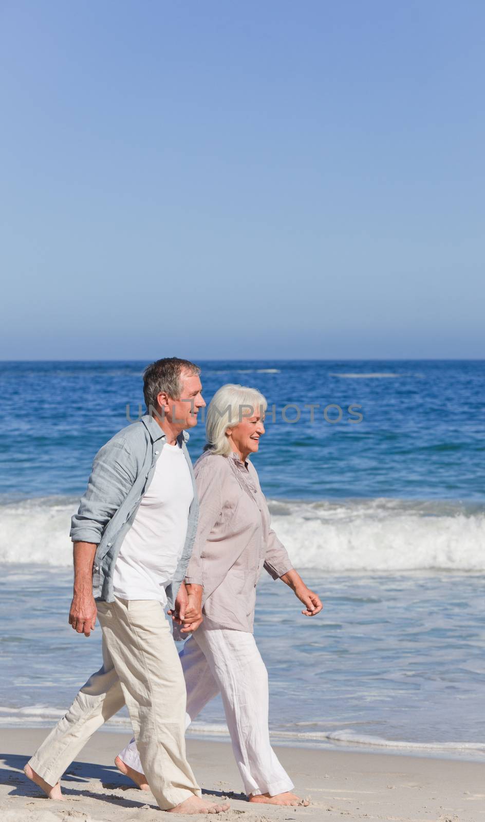 Elderly couple walking on the beach by Wavebreakmedia