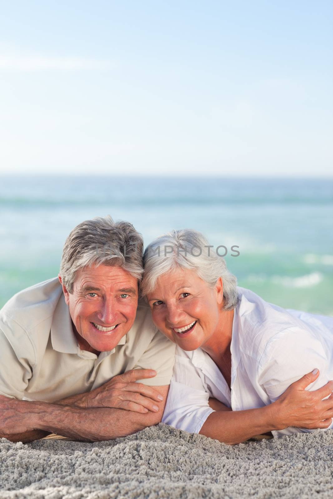 Mature couple lying down on the beach by Wavebreakmedia