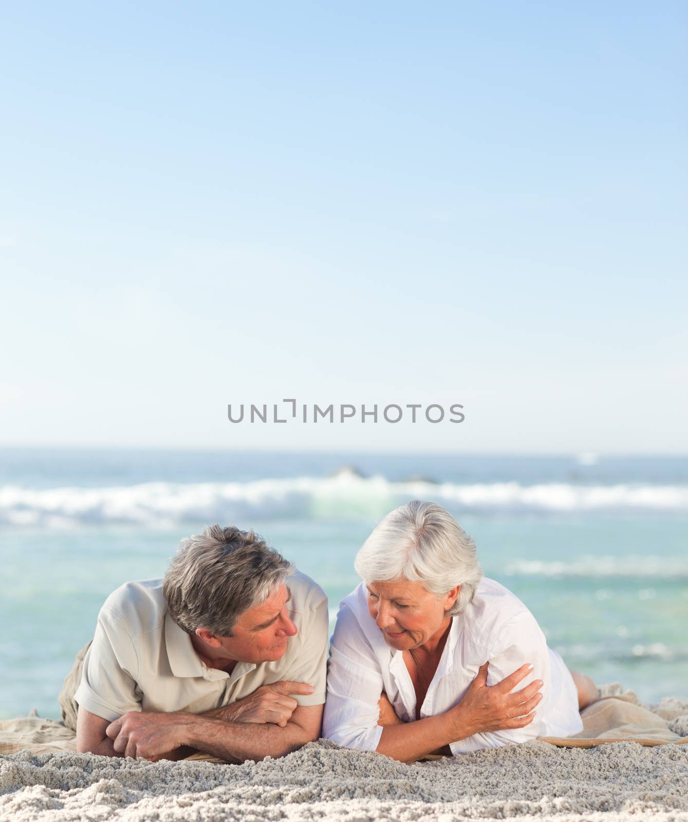 Mature couple lying down on the beach by Wavebreakmedia