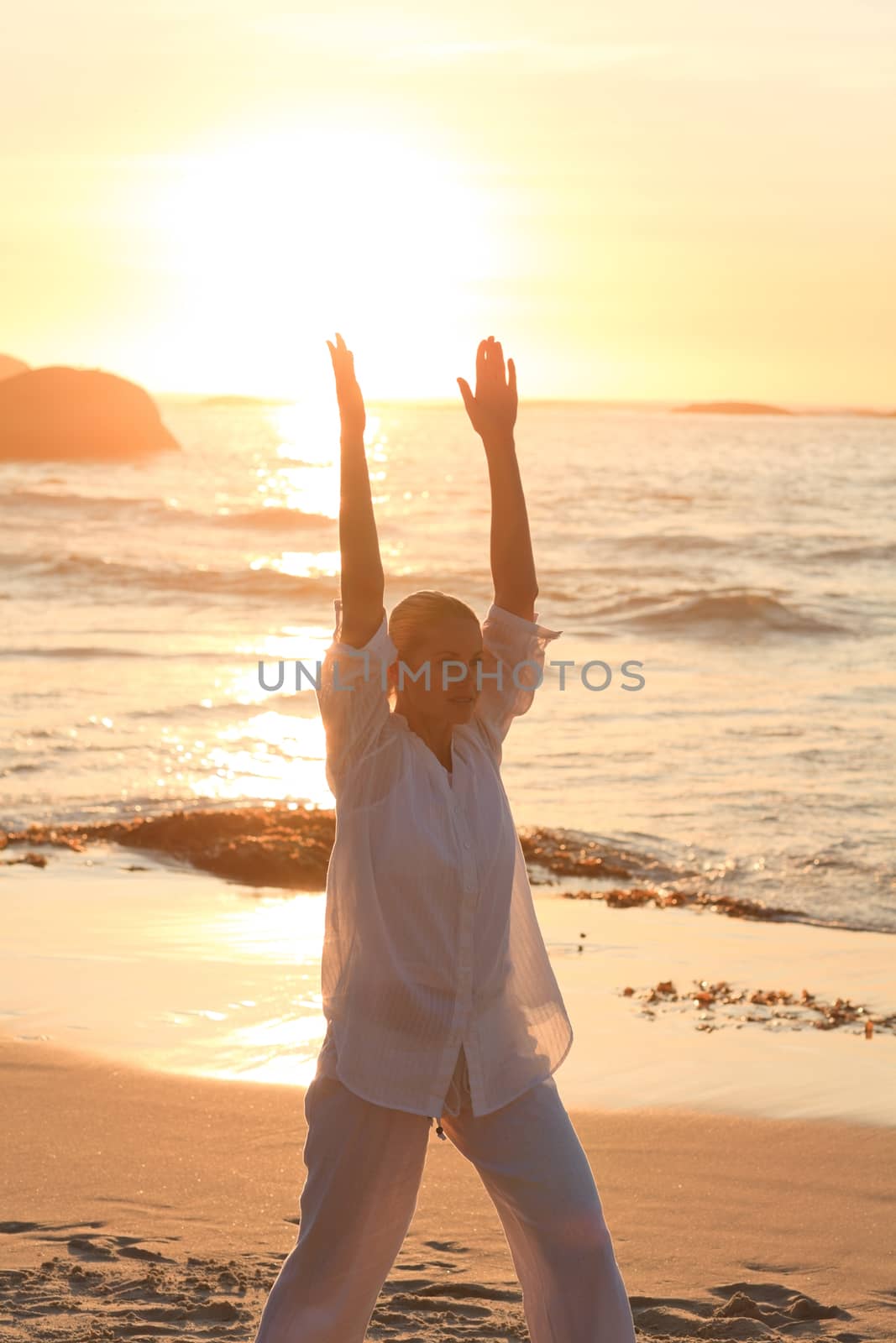 Woman practicing yoga during the sunset against the sea