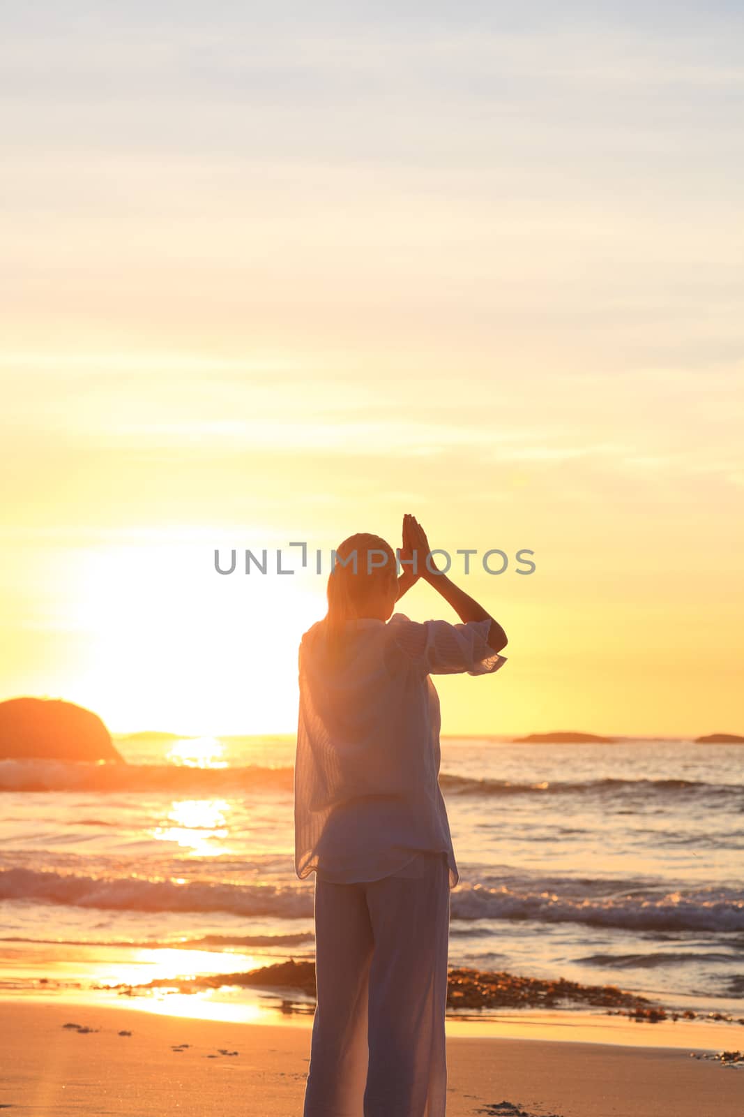 Woman practicing yoga during the sunset at the beach