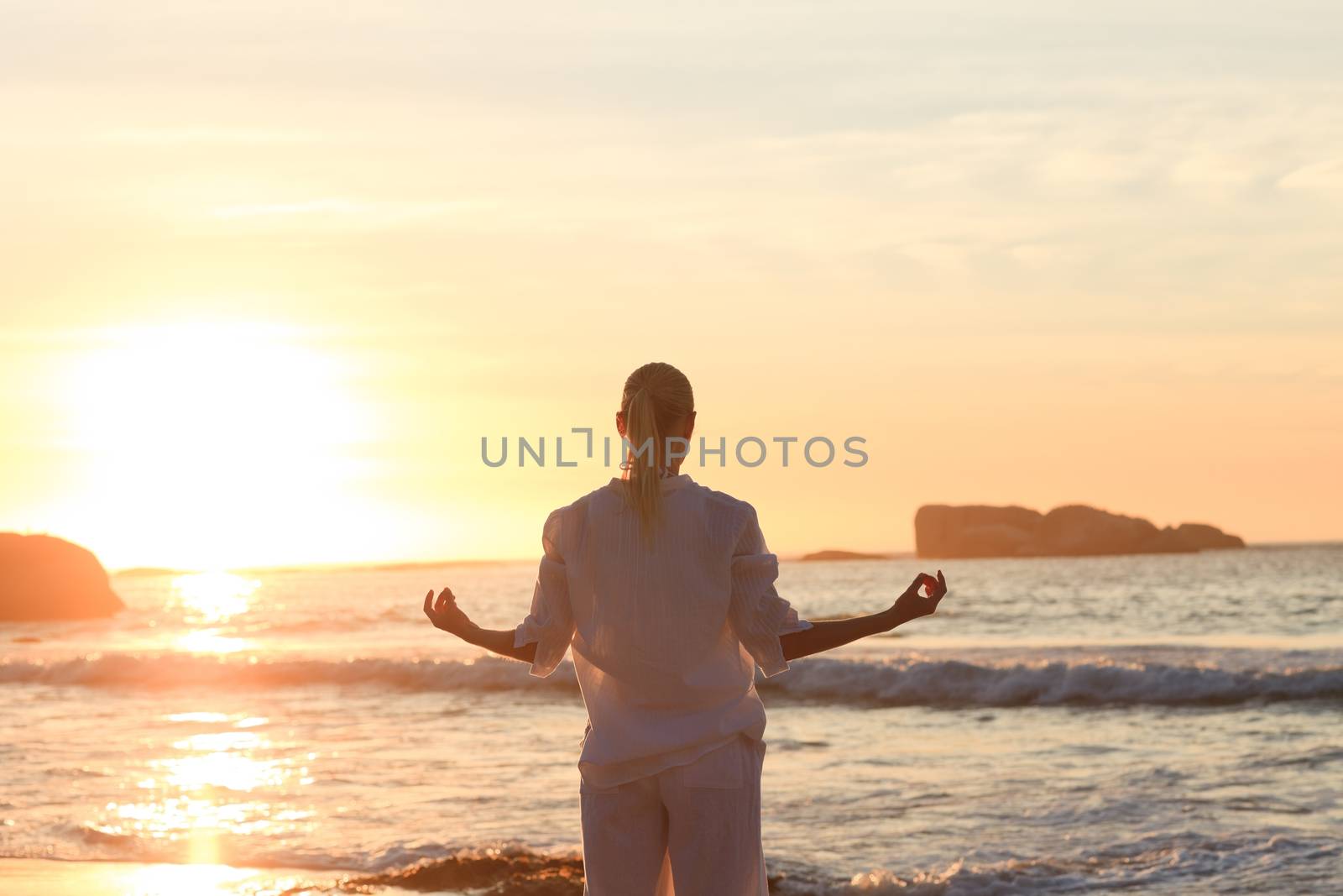Woman practicing yoga during the sunset against the sea