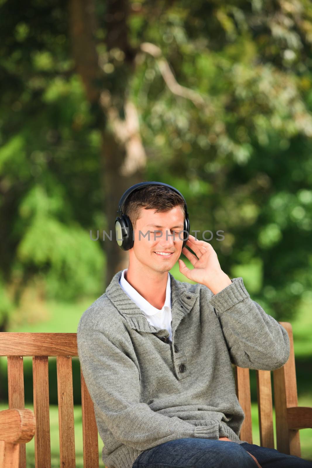 Young man listening to some music on the bench during the summer