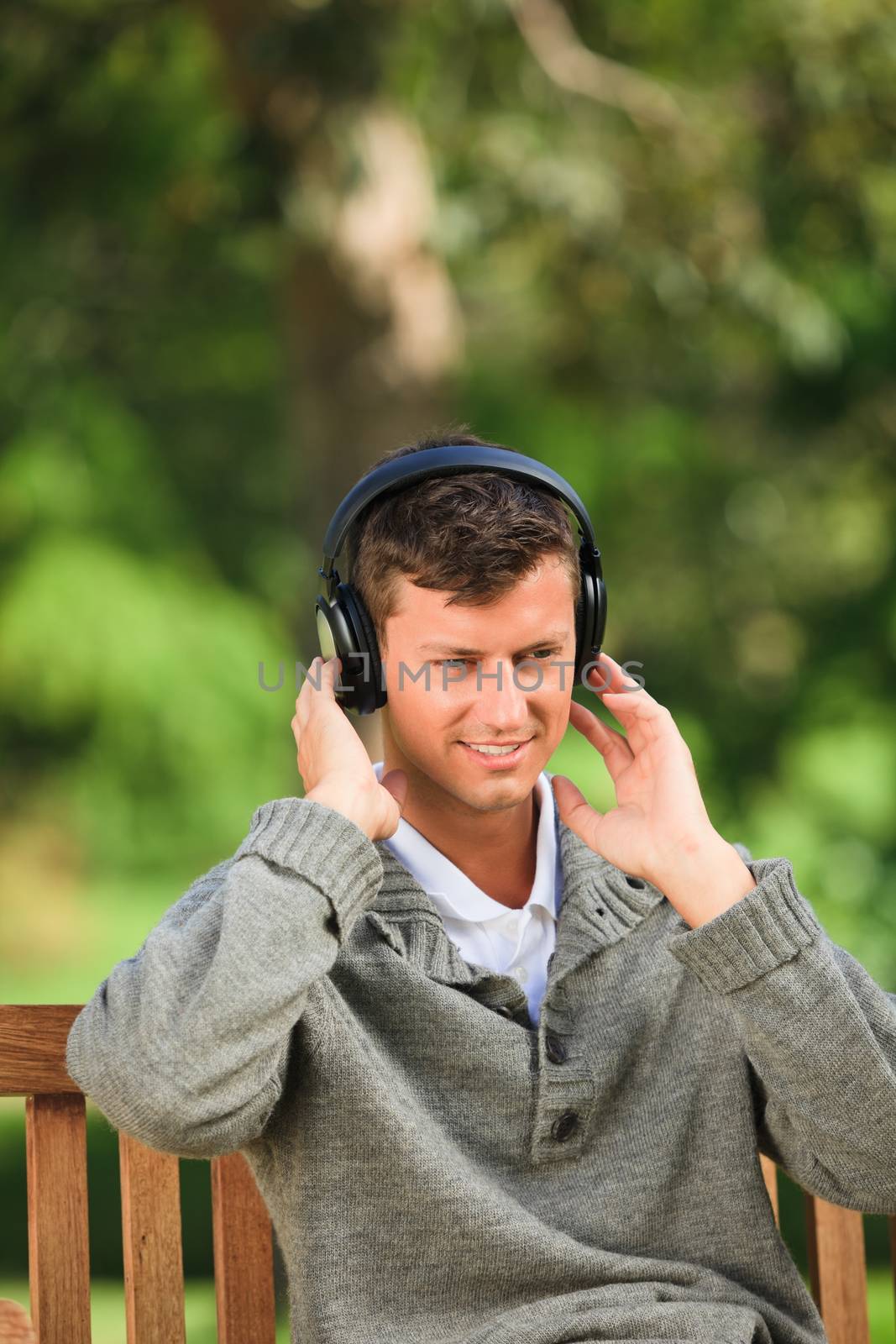 Young man listening to some music on the bench during the summer