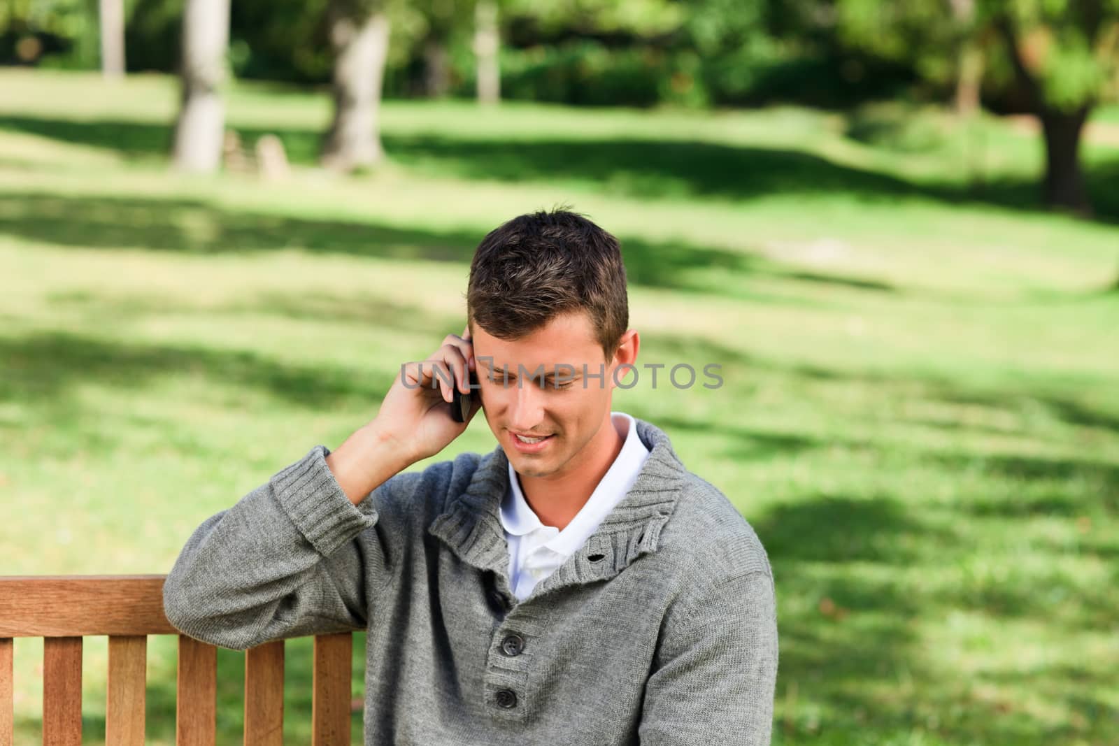 Young man phoning on the bench during the summer 