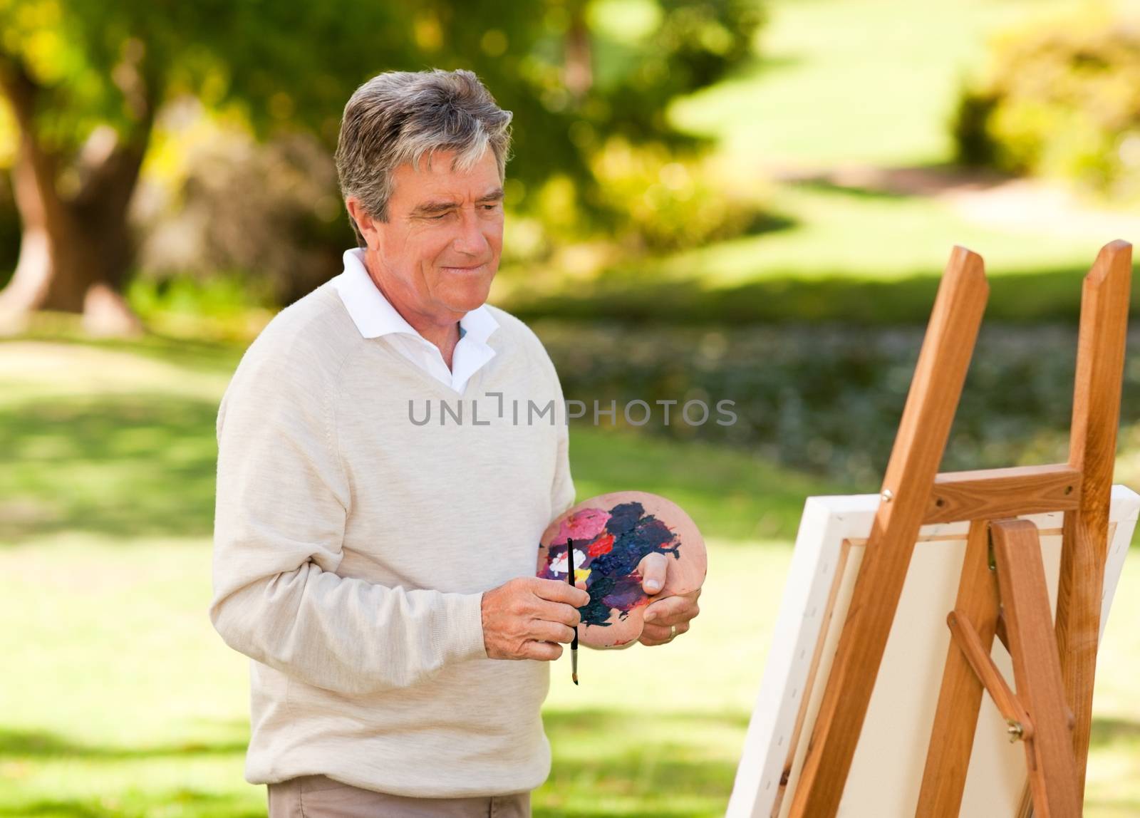 Elderly man painting in the park during the summer