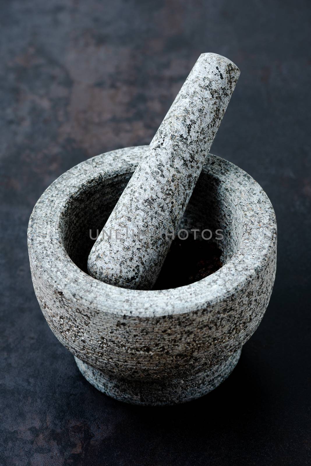 Stone mortar bowl and pestle on dark stone surface by Nanisimova